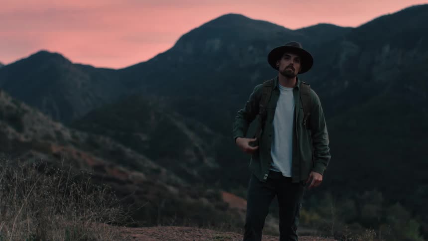 A man stands on the field by the mountains
