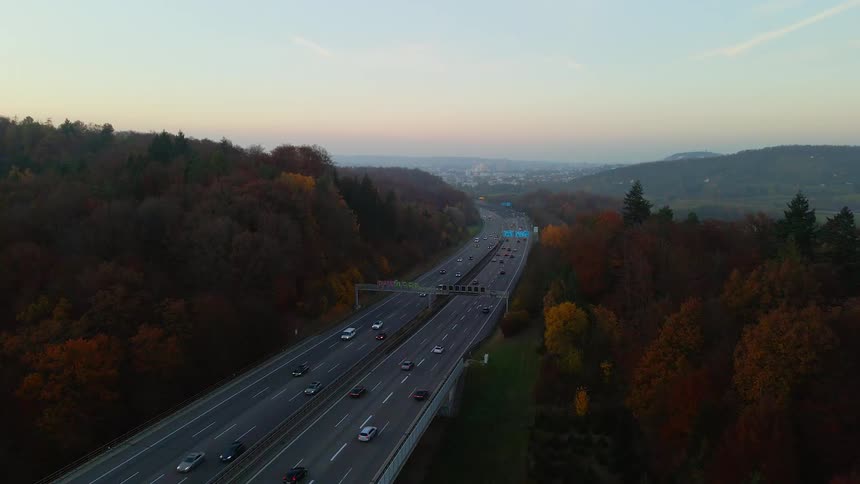 Traffic flows to and from misty city passing autumn trees under red tinted sky