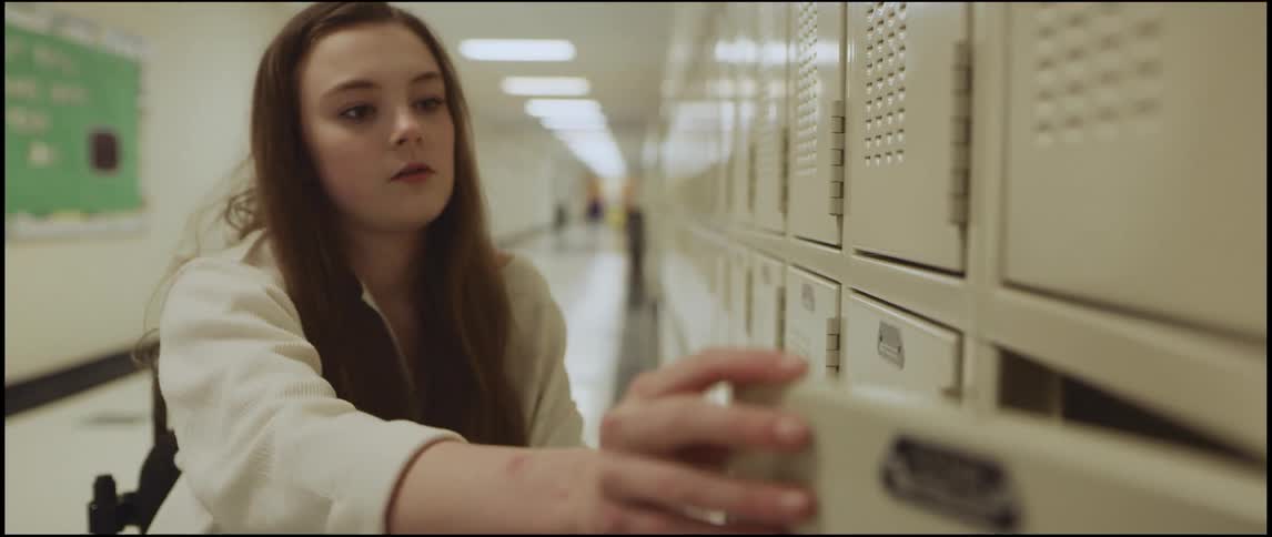 A teenager in a wheelchair takes something out of her school locker and then closes the door and wheels her chair away