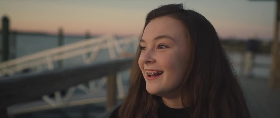 A teenage girl stands on the shore and smiles