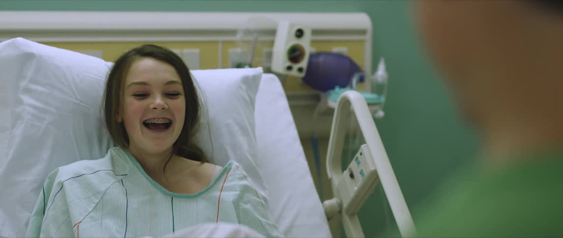 A girl is lying in a hospital bed talking to someone and laughing