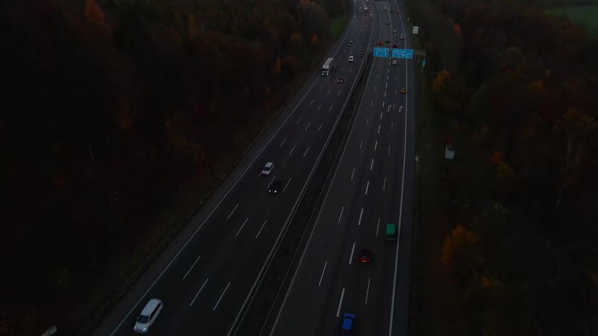 An aerial view of highway traffic in a forested hilly area with a city in the background at dusk