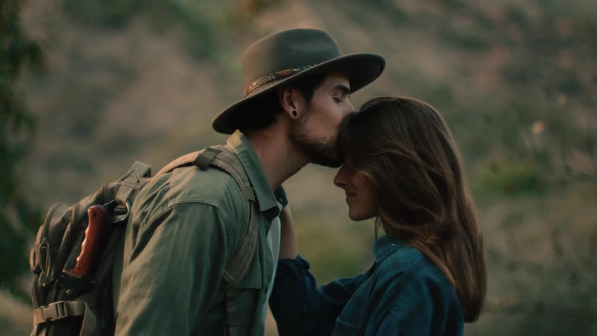 A man says goodbye to a friend with a kiss to her forehead as they both stand outside in the evening