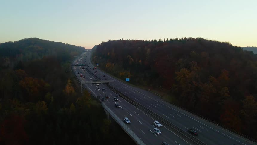 Traffic travels along a freeway through a forested hilltop in the evening