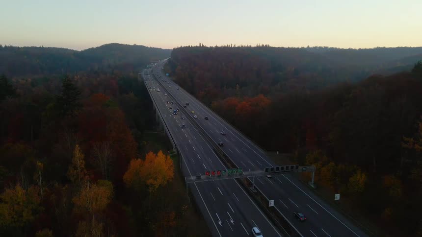 Heavy traffic passes along a busy highway surrounded by lush trees