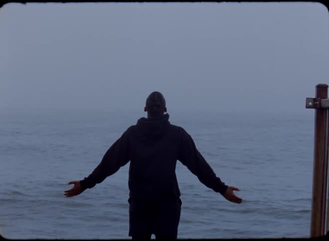 A man is standing at the edge of a pier with his arms out as water splashes in front of him
