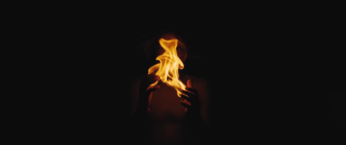 A person opens their hands and the flames of a fire burn in the darkness from the palms of their hands