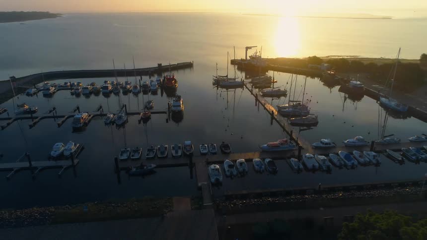 The glowing sun shines on the surface and reflects the boats docked in a marina