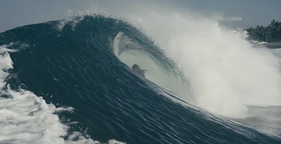 A surfer rides a curling wave to shore shaking his head and hair at the end