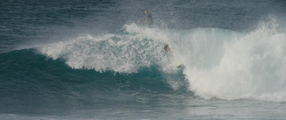 A surfer rides a curling wave while a paddle boarder paddles above