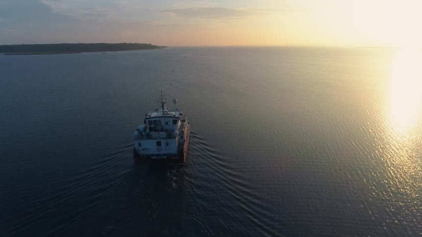 Aerial view of boat traveling across the sea at sunrise