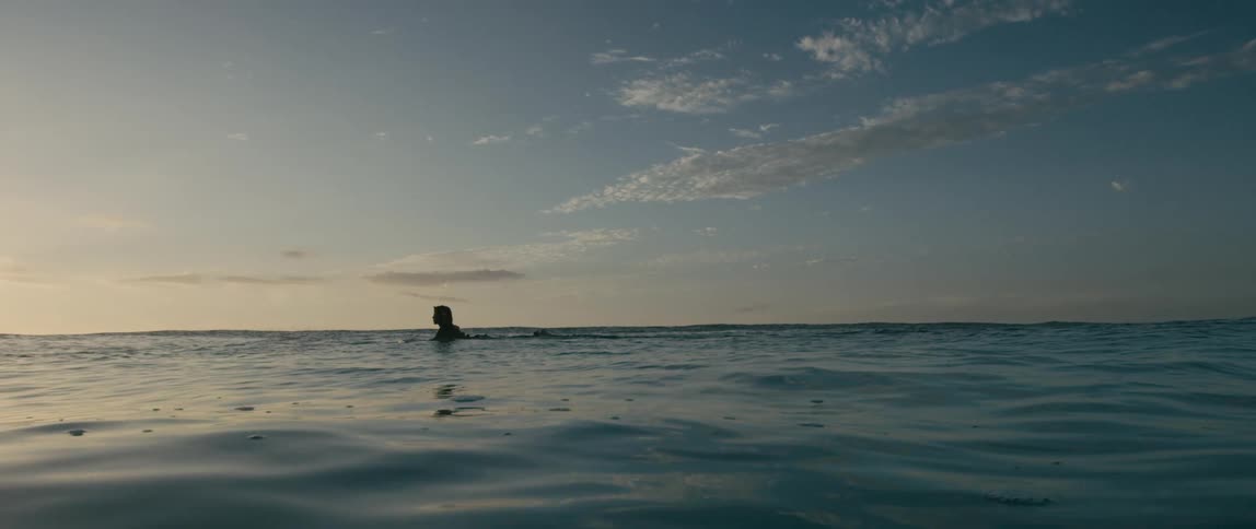 Teen surfer swims on surfboard in sea at dusk