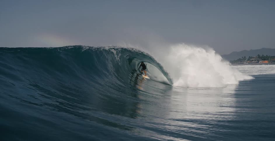 Teen surfer with long hair and wetsuit rides on ocean wave