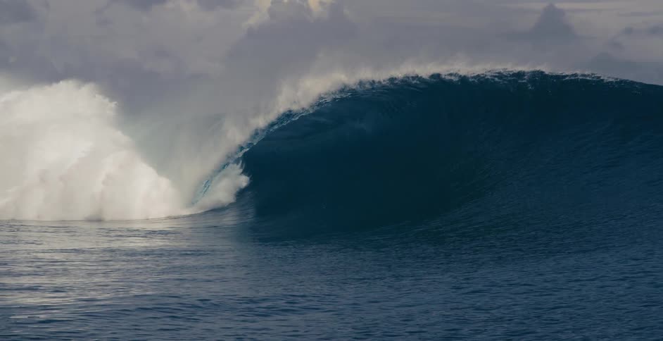 A large wave crashes in the ocean during the day