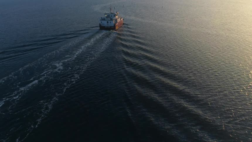 A boat is sailing across the water as the sunlight is reflecting the ripples and waves