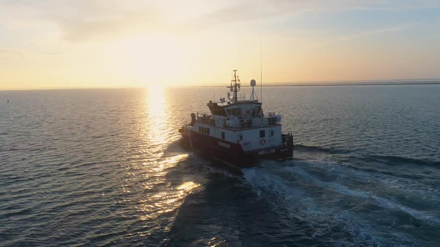 A boat is sailing across the water as the sun is setting in the distance
