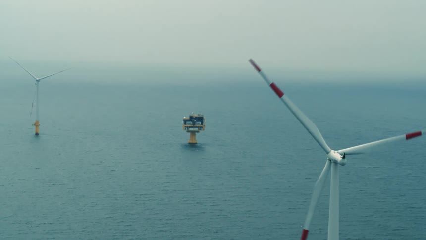 Wind turbines stand in the ocean near a platform on a foggy day