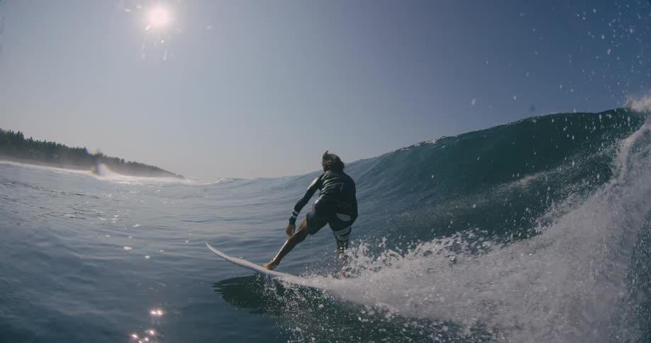 A surfer is riding a big wave with the sun shining brightly in the sky