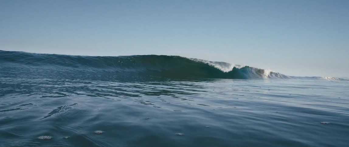 A longwave rolls in and breaks over mostly smooth water