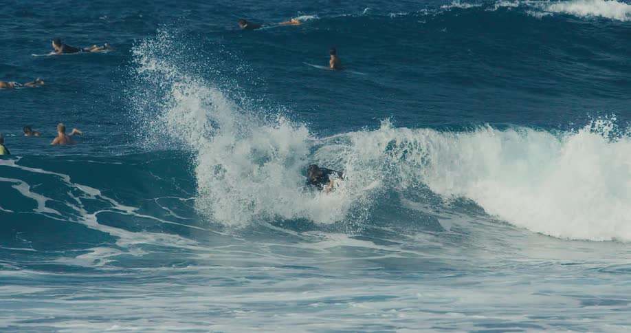 Male surfer with long hair and wetsuit rides on wave