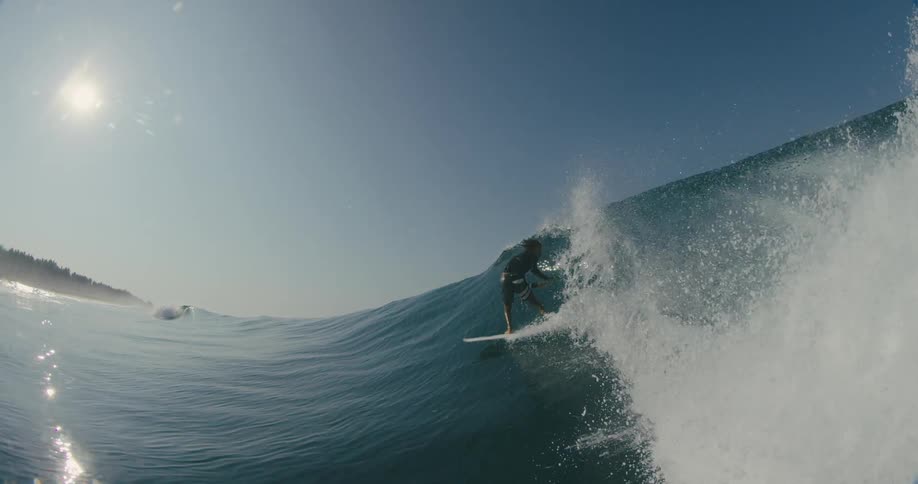 A surfer is riding a big wave with the sun shining brightly in the sky