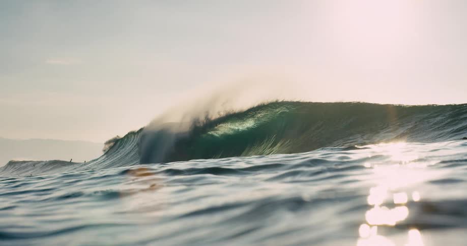 Sunlight is sparkling off water as a wave is crashing over in the ocean