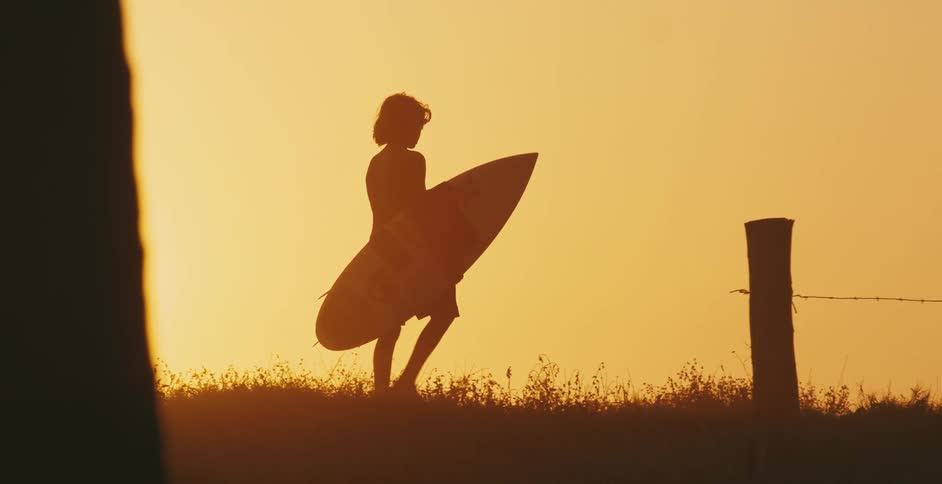 A boy walks on the beach with a surfboard under his arm