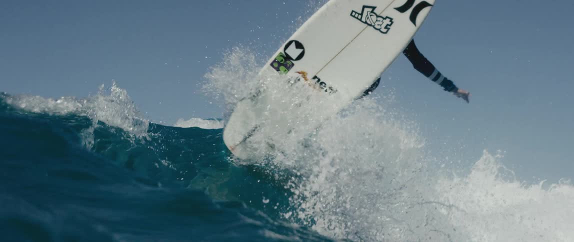 A boy does a jump and spin on a surfboard while surfing on the ocean during the day
