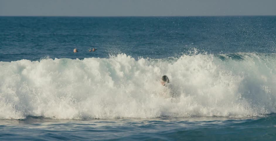 Surfer jumps and spins while riding wave as people float in water in background