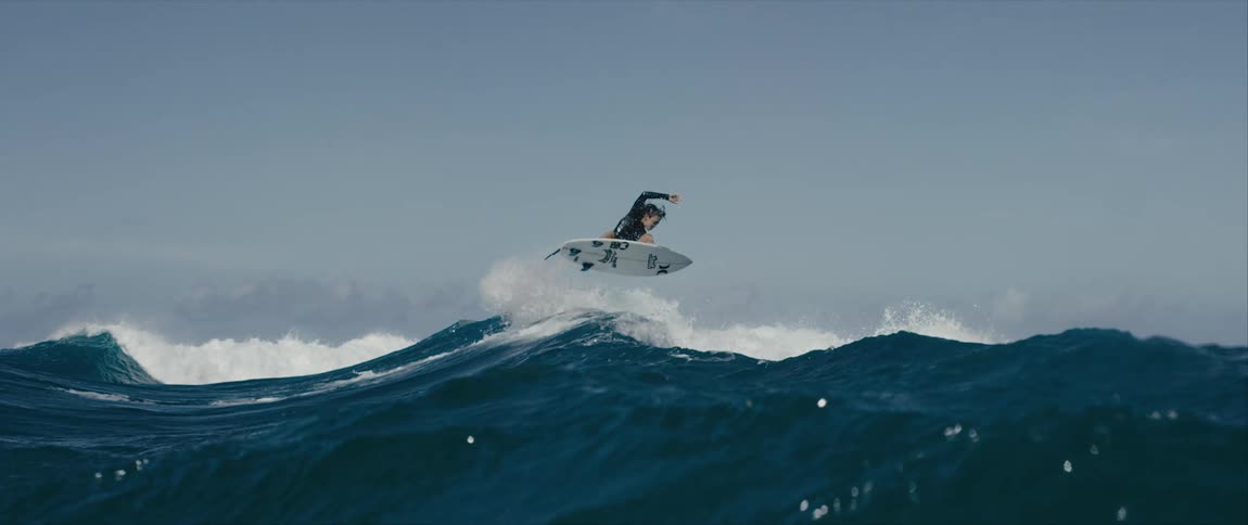 A surfer twirls mid air while riding a breaking wave