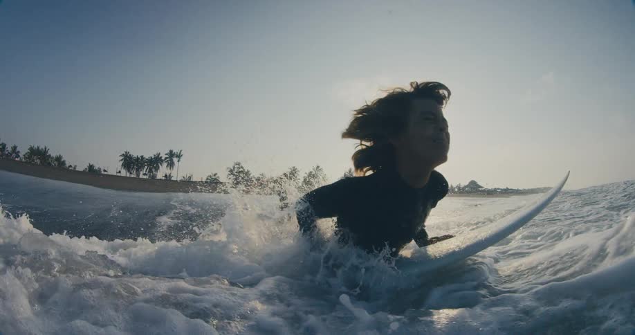 A young male runs in to the ocean and jumps on his surfboard