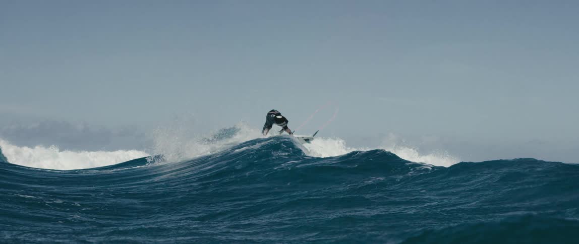 Teen surfer with long hair and wetsuit rides on ocean wave