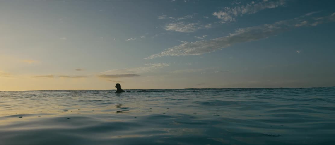 A view of a woman on a surfboard paddling in the ocean