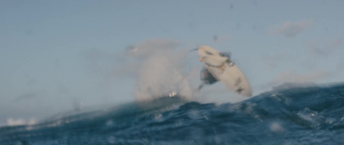 A surfer is riding a big wave and he goes underwater doing a stunt