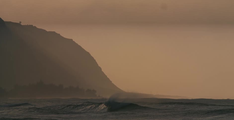 View of ocean waves breaking and distant cliff at bay at dusk