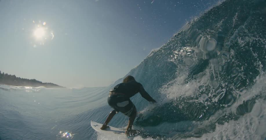 A surfer rides a wave with his arm out for balance