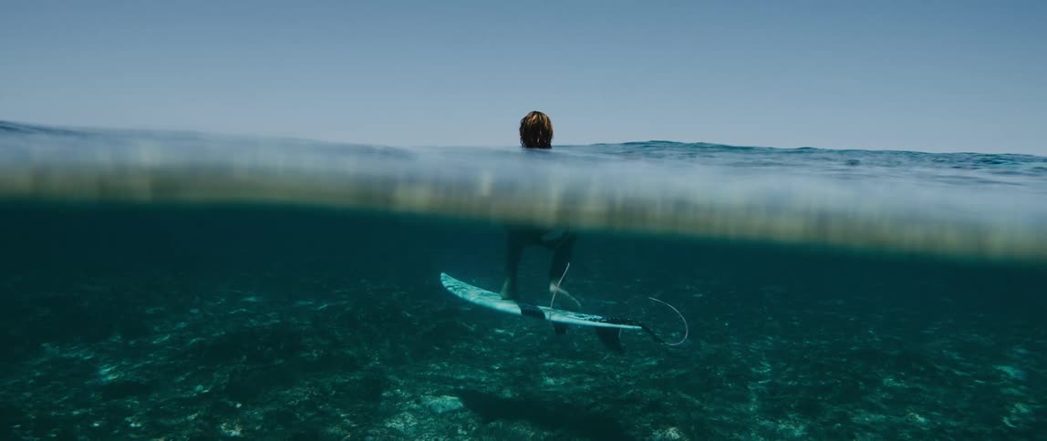 A surfer is underwater on his surfboard with only his head above water
