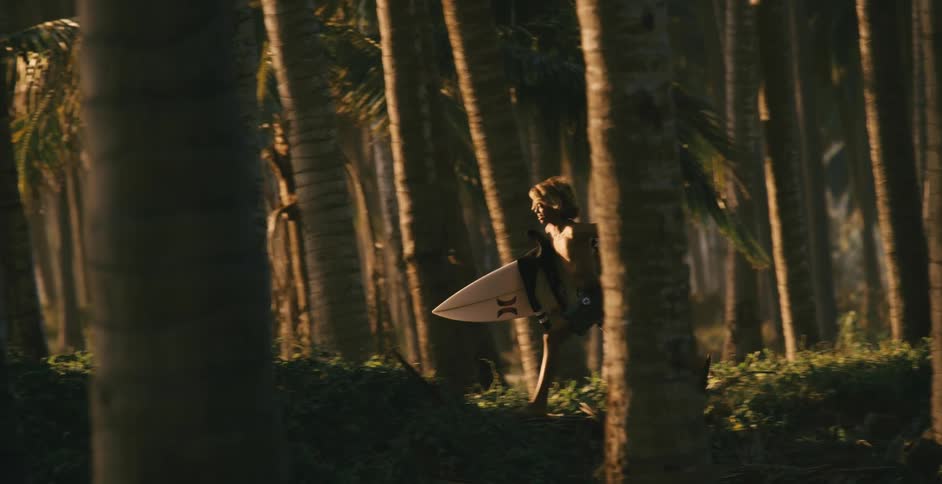 A boy is running through the forest carrying a surfboard