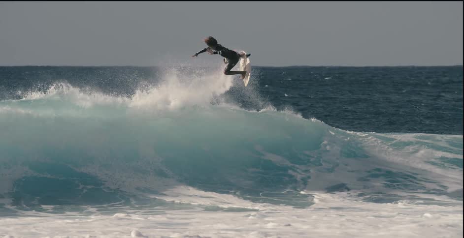 A surfer is riding a big wave as he leaps into the air and does a 360 degree spin with his surfboard
