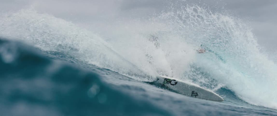 Male teenager surfer with long hair and wetsuit rides on wave
