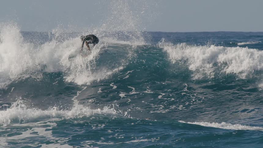 Teen surfer with long hair and wetsuit rides on wave