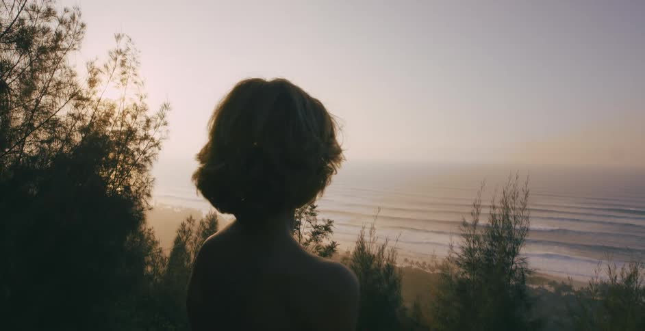 A young boy stands on the shore and looks at the water