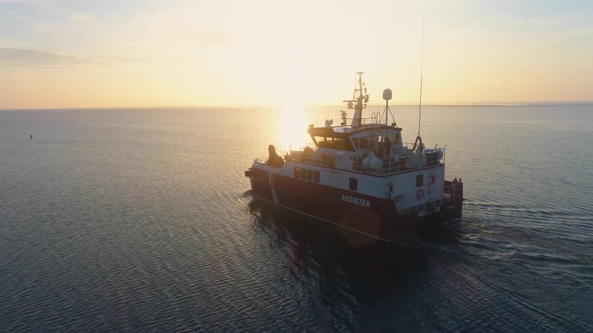 A support ship named the assister travels through the water near the coast at sunset