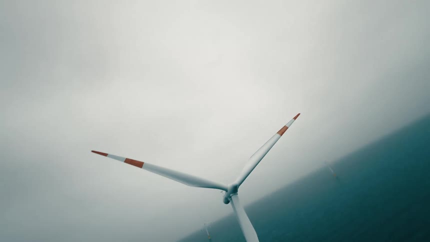 A spinning wind turbine on the ocean on a cloudy day