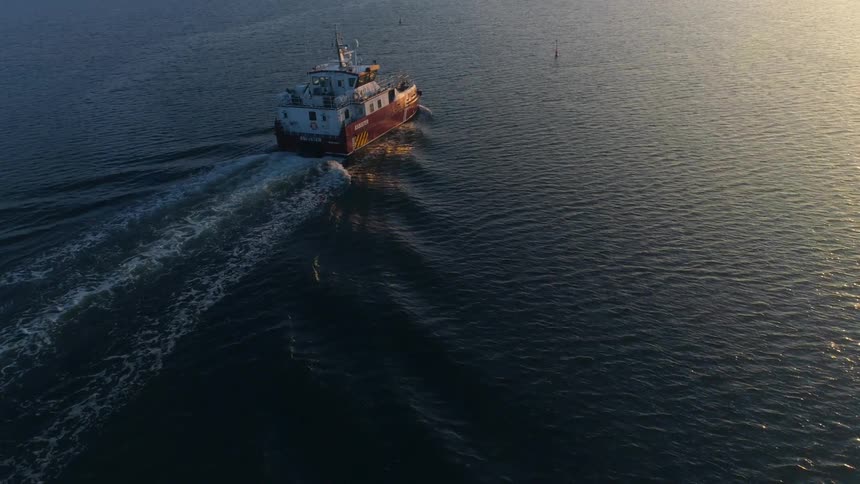 A boat is sailing across the water as the sunlight is reflecting the ripples and waves
