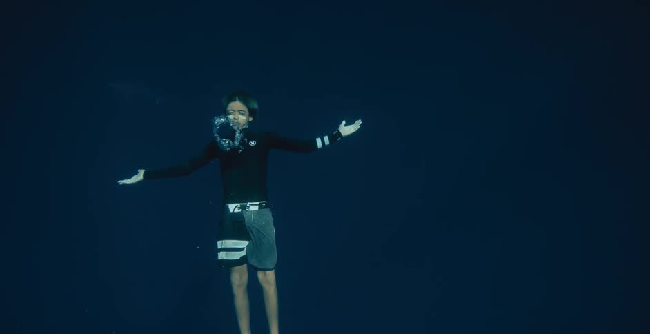 A boy blows bubbles in the water and he raises his arms to his side and sinks