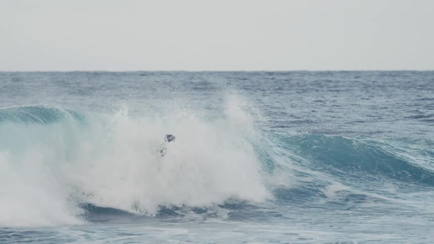 A surfer twirls and turns midair while riding a curling breaking wave