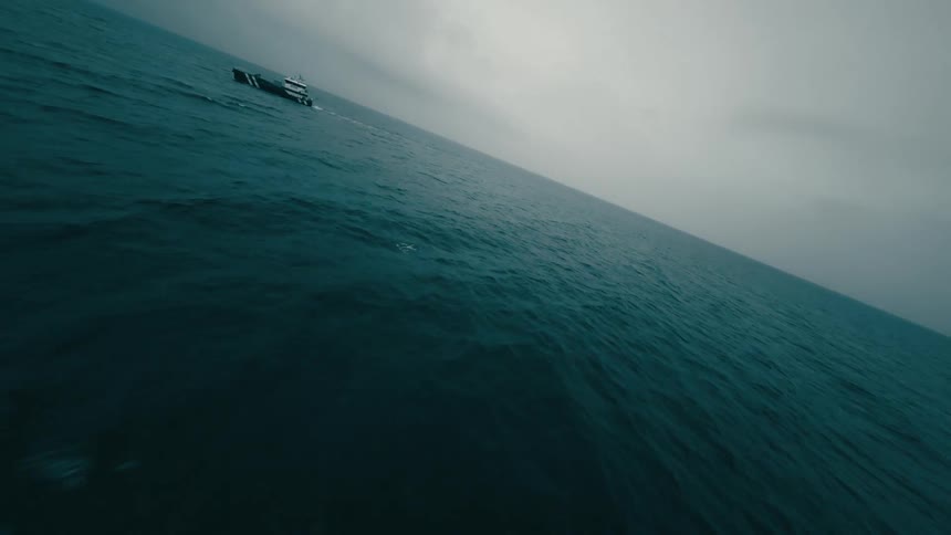 A large boat sailing in the ocean towards wind turbines