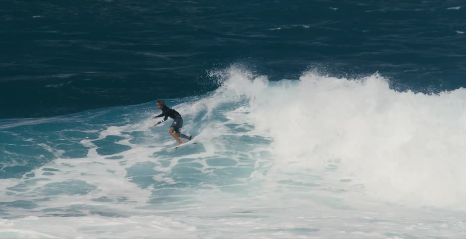 Teen surfer with long hair and wetsuit rides on ocean wave