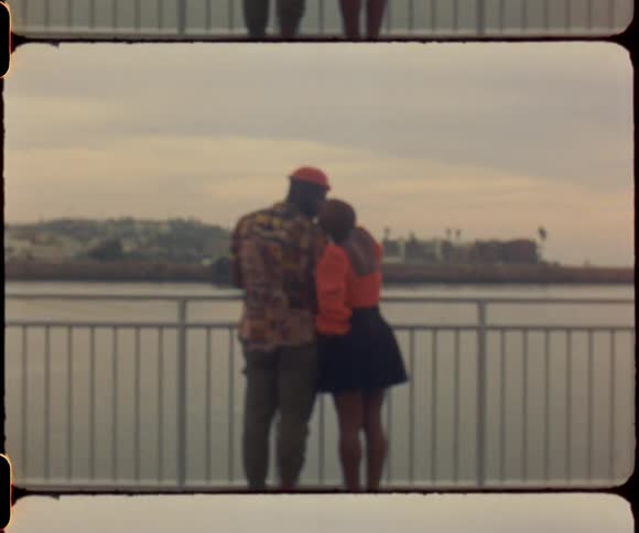 Couple stand by rail overlooking water kissing and hugging